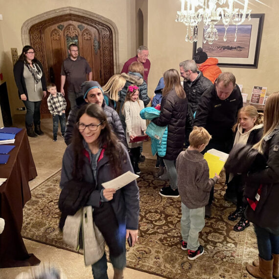 A group of students and parents check in for an evening event. Architectural details including a stone archway, intricately carved wooden doors and a crystal chandelier decorate the entryway of the Mansion.