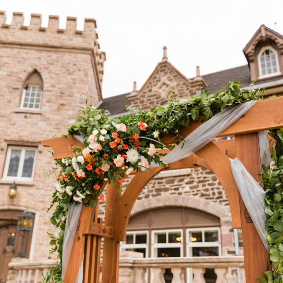 A wooden arch draped with flowers, greenery and tulle in front of the Mansion's castle-like exterior.
