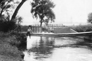 A historical photo of the High Line Canal with a person sitting near a wooden bridge.