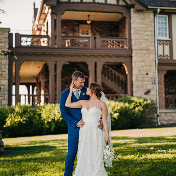 A bride and groom pose for a portrait with the tudor-style West balcony and porch of the Mansion in the background.