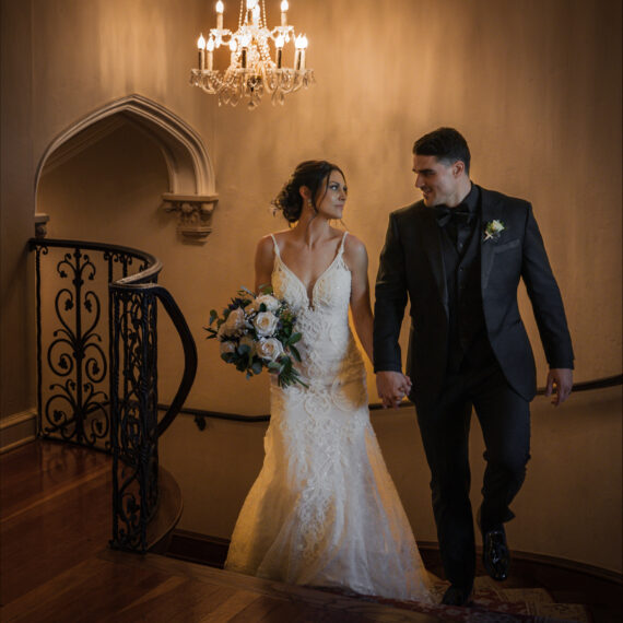 Bride and groom walk hand-in-hand up the spiral staircase.