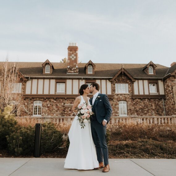 A groom kisses his bride's check in front of the Mansion grounds.