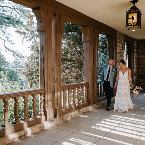 A bride and groom walk hand-in-hand along the west balcony.