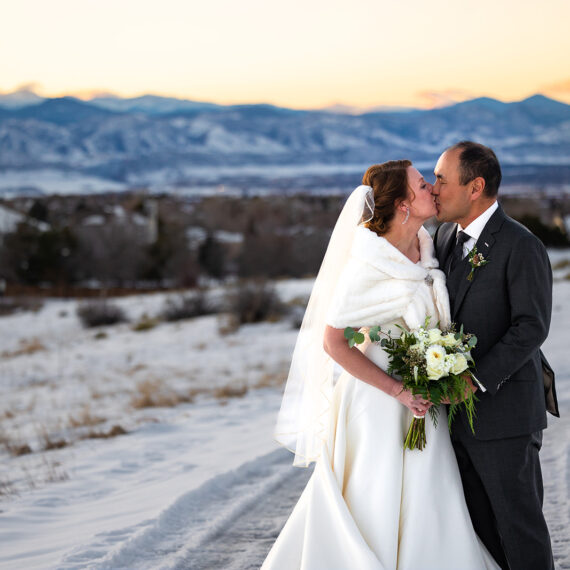 A bride and groom exchange a kiss on the Mansion grounds with snowy mountains in the background.
