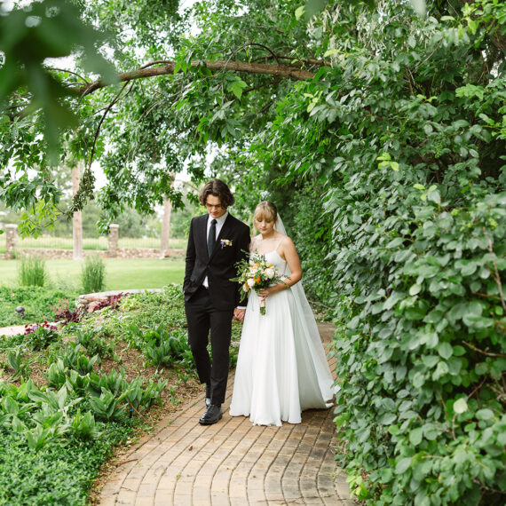 A bride and groom walk along a path in Marian's Garden.