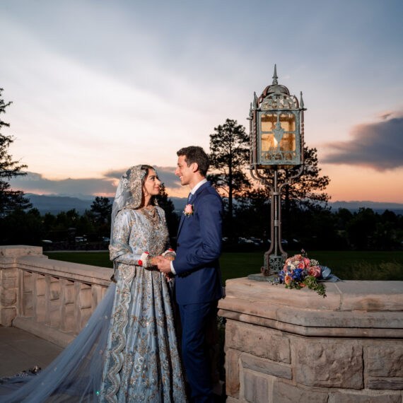 A bride and groom hand-in-hand on the front porch of the Mansion during sunset.