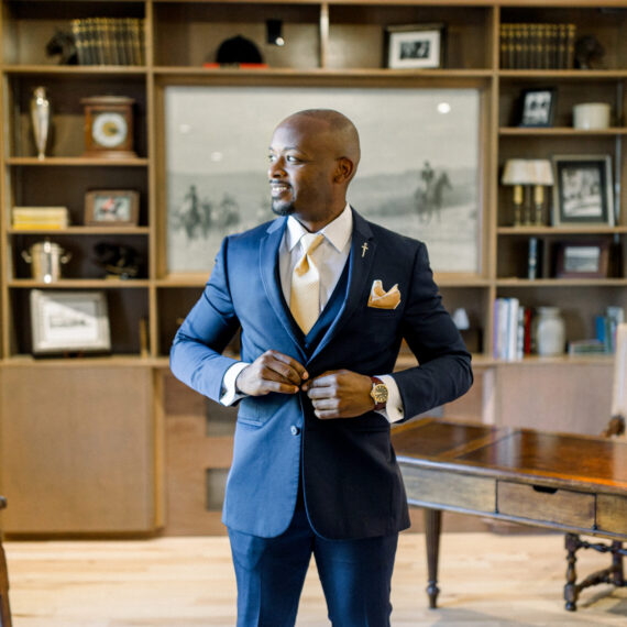 A groom stands in front of the Historic Lounge bookcase.