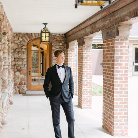 A groom stands underneath the covered back patio at the Mansion posing for a portrait.