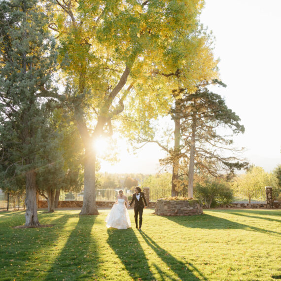 Bride and groom walk in the back yard of the Mansion through fall leaves.