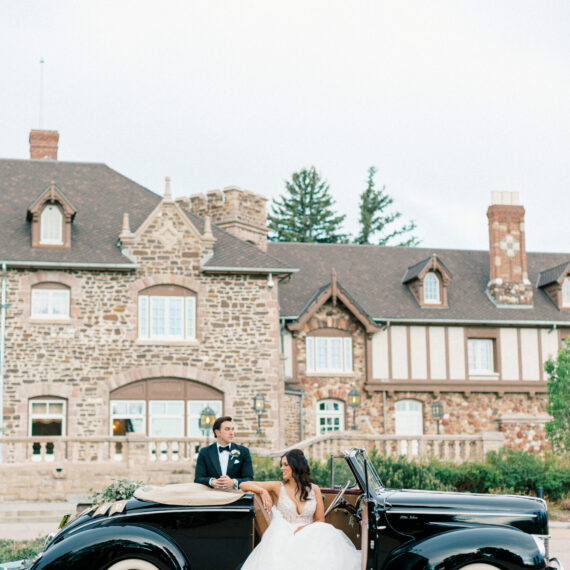 Bride and groom pose in a vintage car on the circle drive of the Mansion.