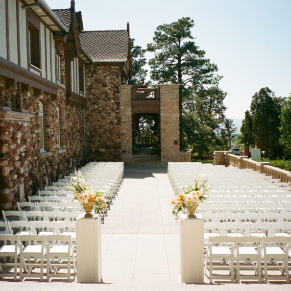The front Veranda set up for a ceremony with white folding chairs and floral pillars at the start of the aisle.